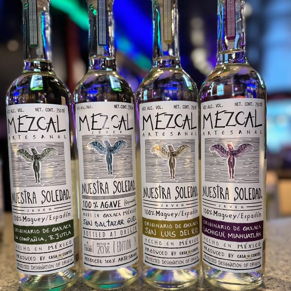 Four bottles of Nuestra Soledad Mezcal, a Mexican spirit, displayed in a row.