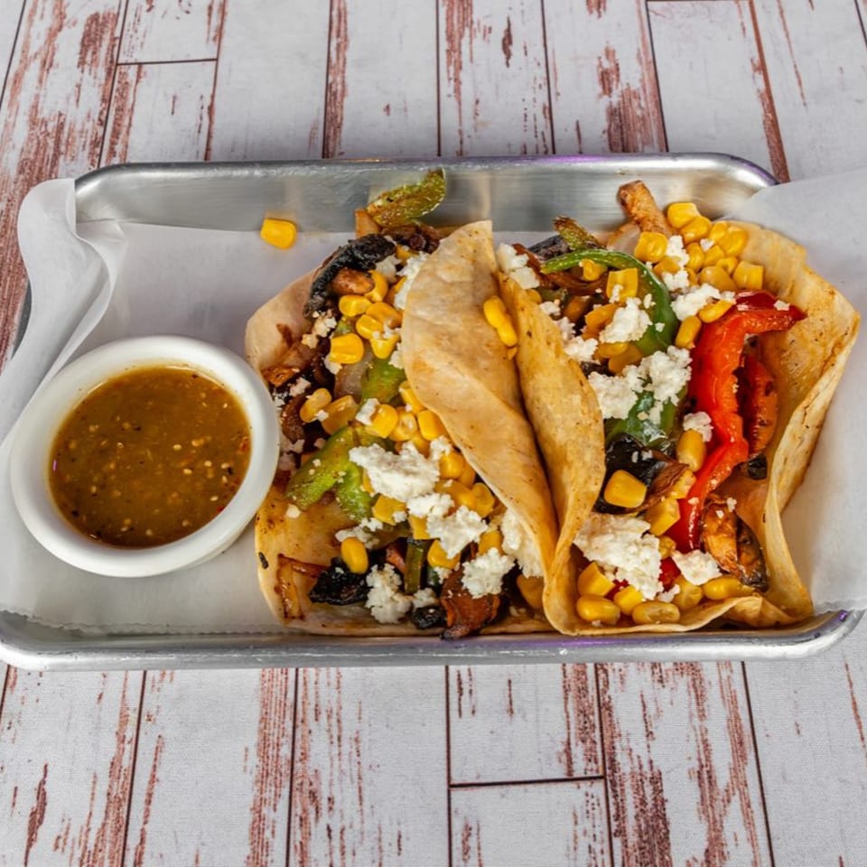 Two Lomeli's Mexican Bar and Grill tacos filled with corn, peppers, and cheese, with a side of salsa.