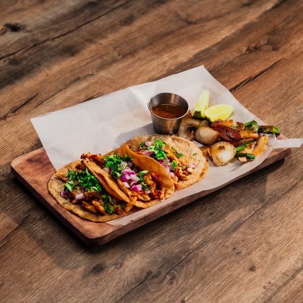 Two Lomeli's Mexican Bar and Grill tacos with grilled vegetables, lime, and sauce on a wooden board.