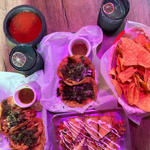 An overhead view of Lomeli's Mexican Bar and Grill's tacos, chips, salsa, and drinks on a wooden table.