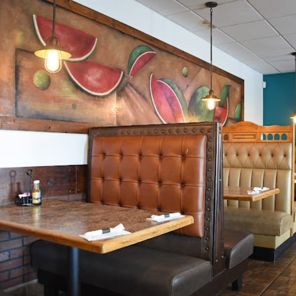 Interior of Lomeli's Mexican Bar and Grill with brown leather booths, wooden tables, and a colorful watermelon mural.
