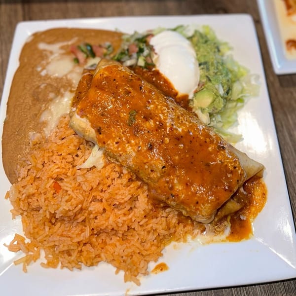 A Lomeli's Mexican Bar and Grill burrito covered in red sauce, with rice, beans, and salad.