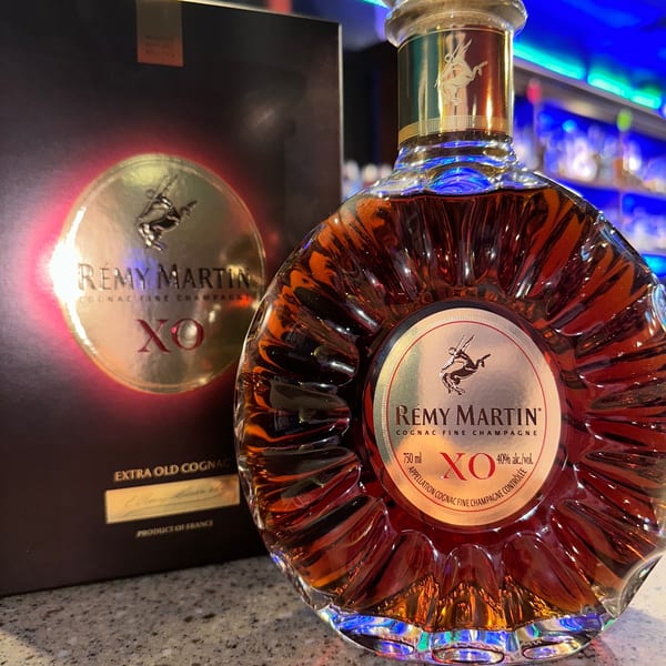 A bottle of Rémy Martin XO cognac and its box on a counter with a blurred bar in the background.