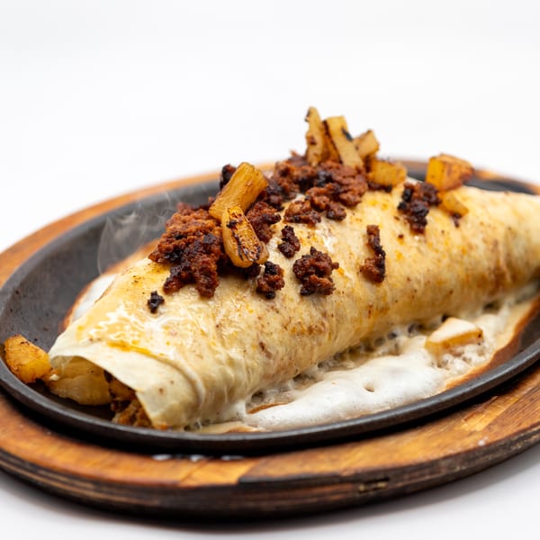 Steaming Lomeli's Mexican Bar and Grill burrito topped with chorizo and potatoes, served on a sizzling platter.