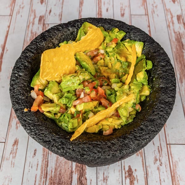 Fresh guacamole with chunky avocado, diced tomatoes, onions, and tortilla chips in a dark stone bowl.