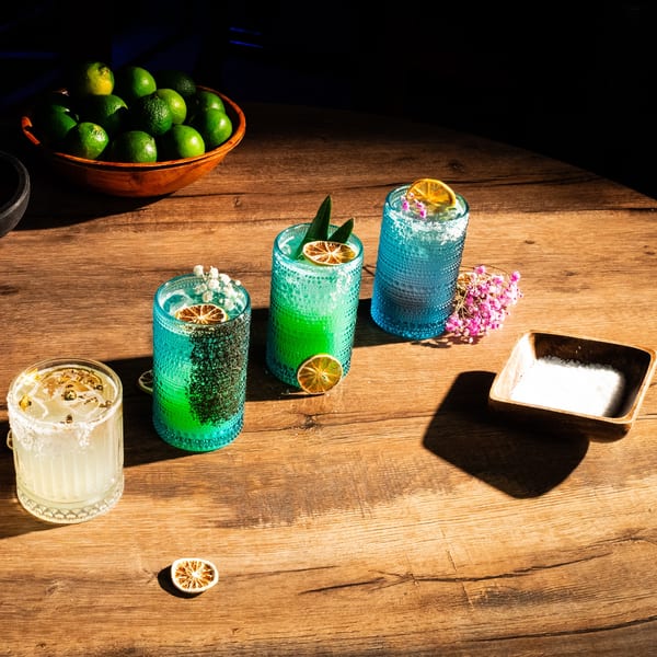 Four vibrant Lomeli's Mexican Bar and Grill cocktails and a bowl of limes on a wooden table.