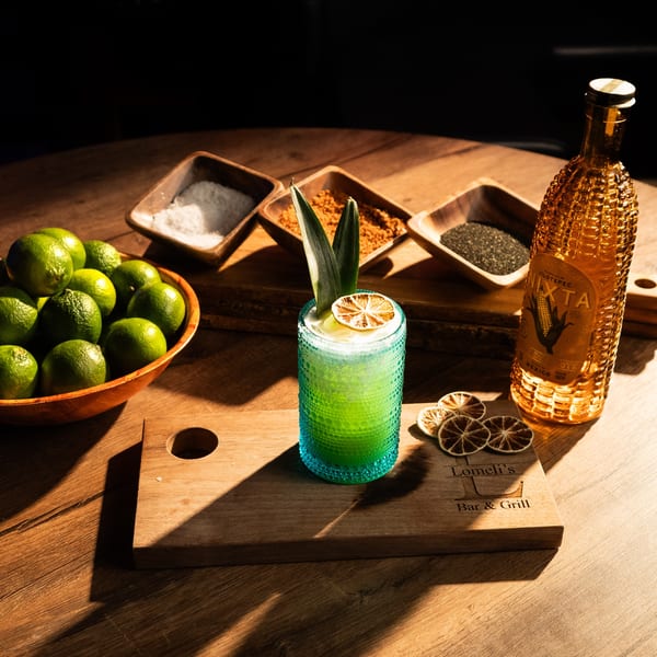 Lomeli's Mexican Bar and Grill cocktail with limes, spices, and a decorative bottle on a wooden table.