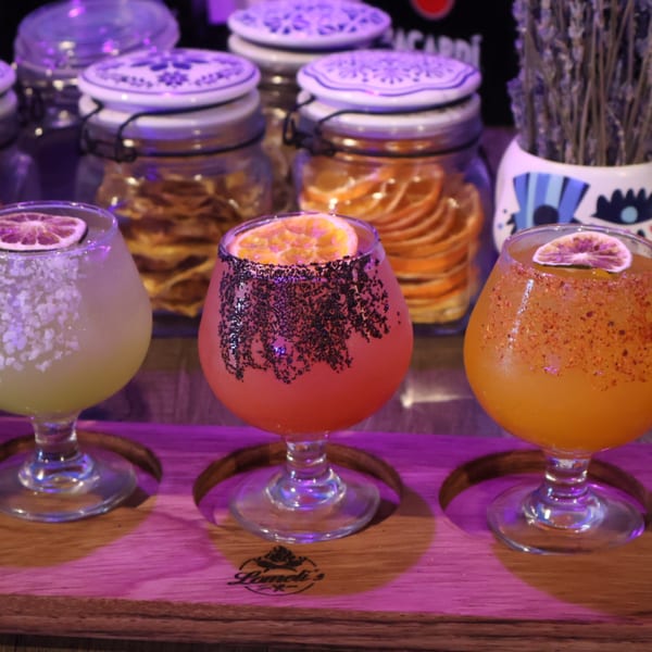 Three colorful Lomeli's Mexican Bar and Grill cocktails with fruit garnishes on a wooden tray.