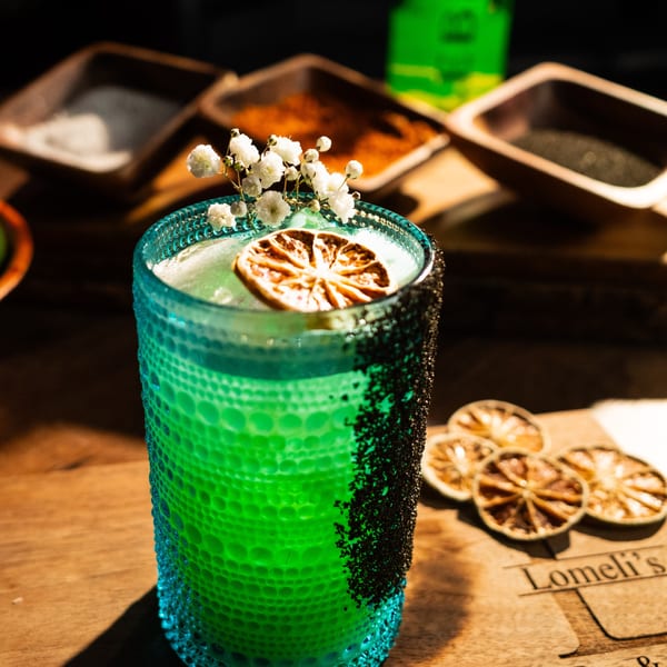 A vibrant green Lomeli's Mexican Bar and Grill cocktail with a dried orange slice and baby's breath.