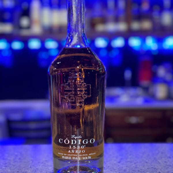 A bottle of Código 1530 Añejo tequila stands on a bar with blue lighting.
