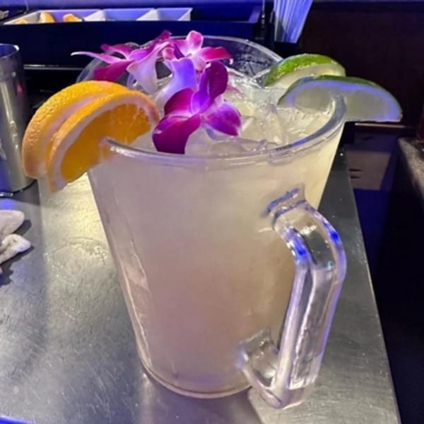 A large pitcher of Lomeli's Mexican Bar and Grill margarita, garnished with orange, lime, and orchids.