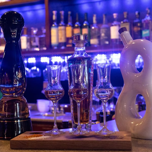 Three tequila glasses and bottles on a wooden tray with salt and chili powder at Lomeli's.