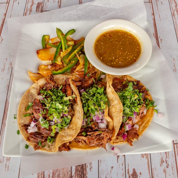 Three Lomeli's Mexican Bar and Grill tacos with meat, cilantro, and onions, served with salsa and peppers.