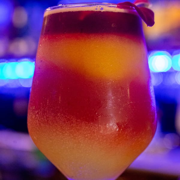 A vibrant, layered Lomeli's Mexican Bar and Grill drink with red, orange, and yellow hues, garnished with a red leaf.