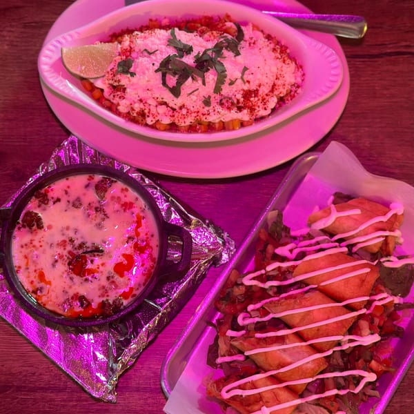 Three Mexican dishes on a wooden table, including elote, queso fundido, and taquitos.
