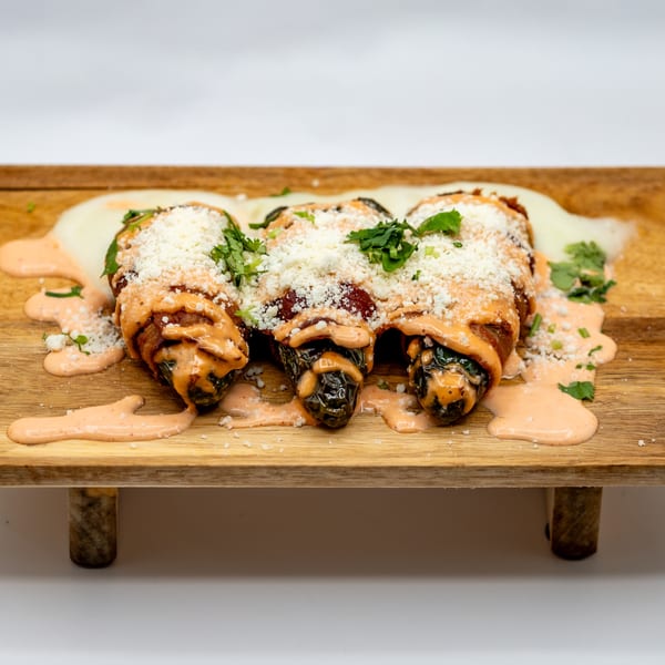 Three Lomeli's Mexican Bar and Grill jalapeño poppers on a wooden board, drizzled with sauce and cheese.