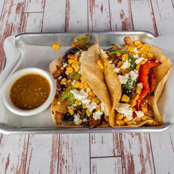 Two Lomeli's Mexican Bar and Grill tacos with corn, peppers, and cheese, served with a side of salsa.