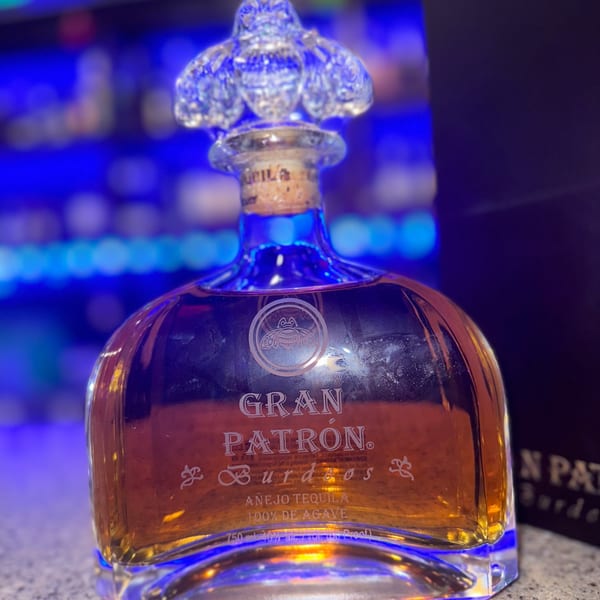 A bottle of Gran Patrón Burdeos Añejo Tequila with a decorative stopper, glowing with blue light.