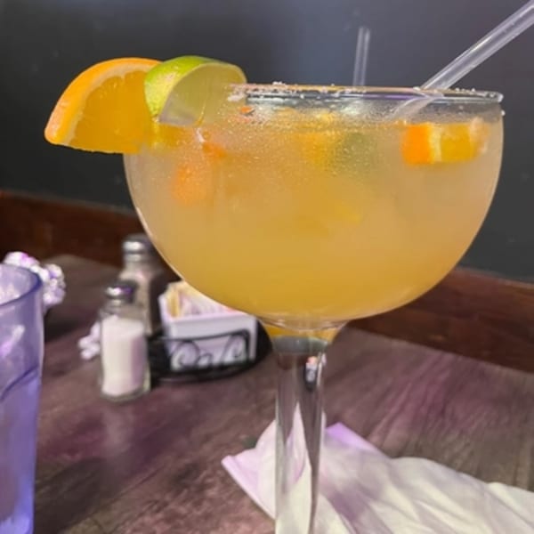 A large, frosty margarita with orange and lime slices, and a salted rim, on a wooden table.